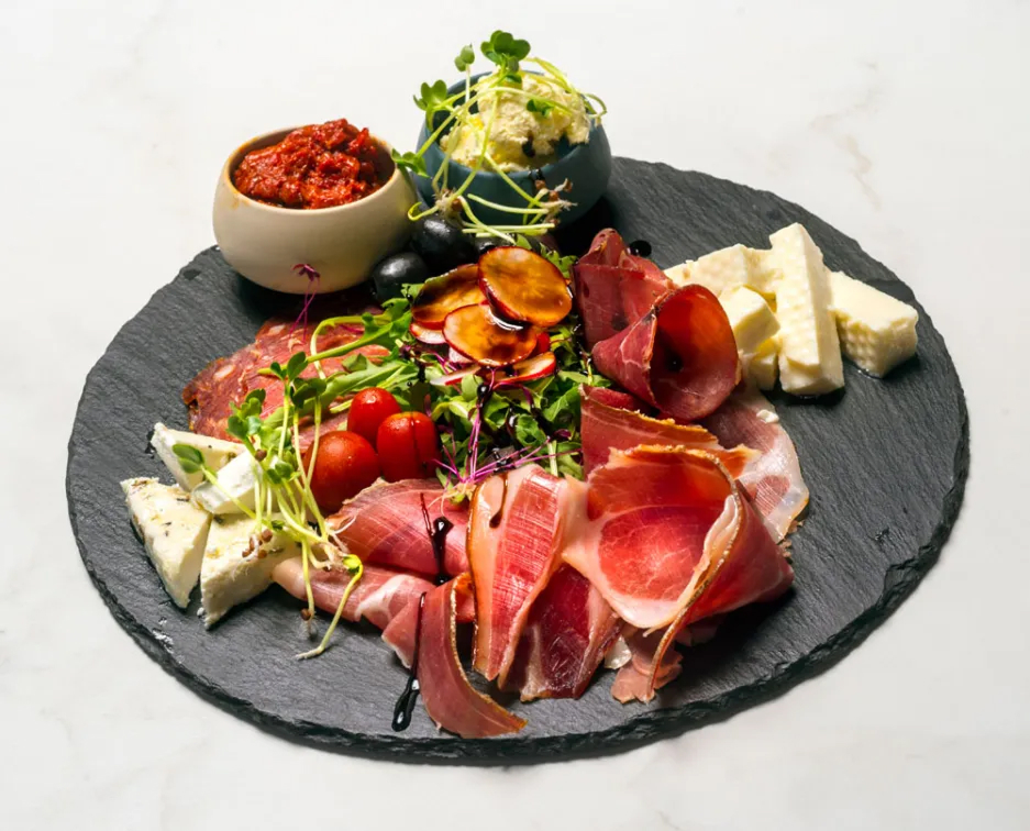 Charcuterie board of meats, cheeses, vegetables, and spreads.