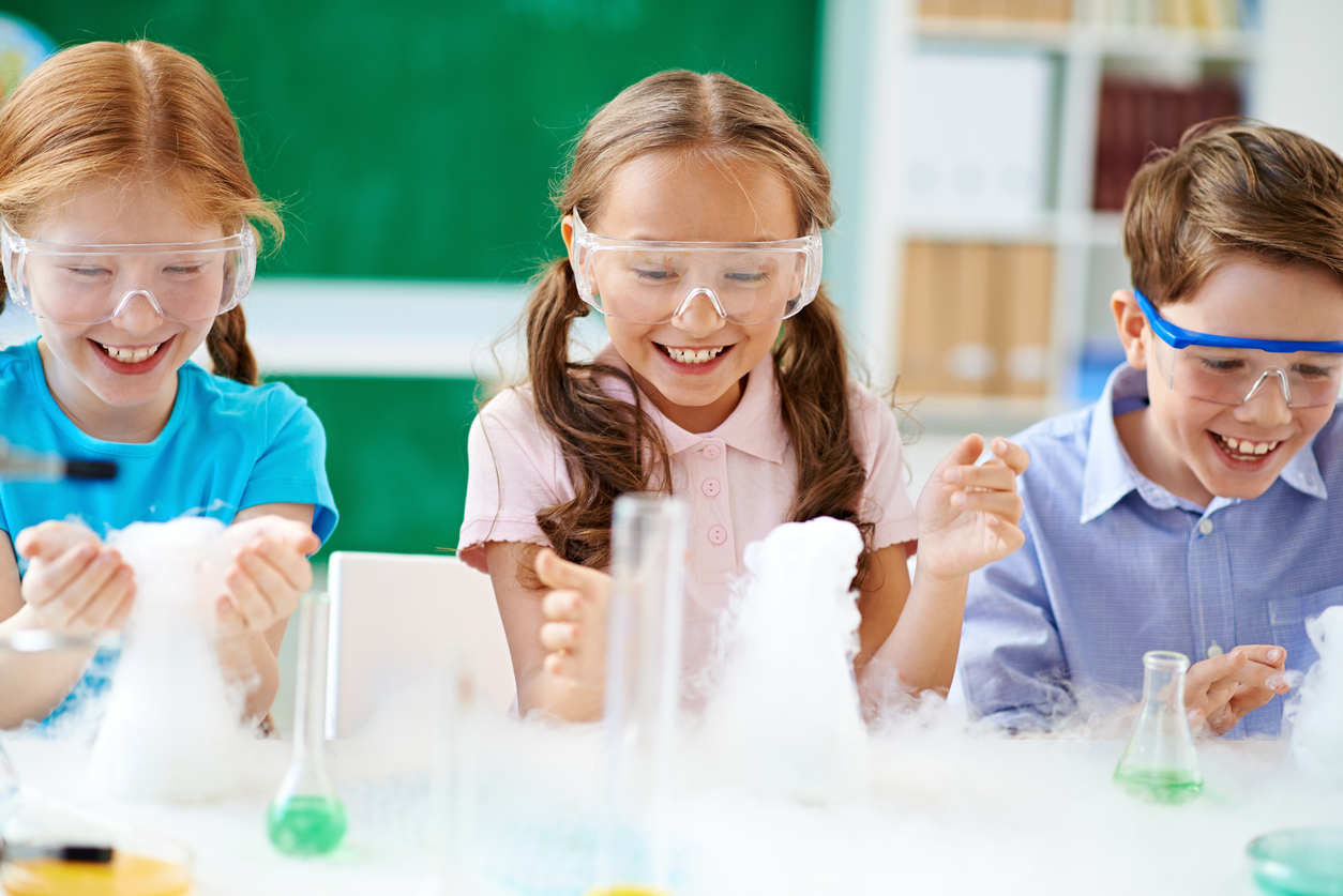 Cheerful elementary students observing chemical reaction with smoke.