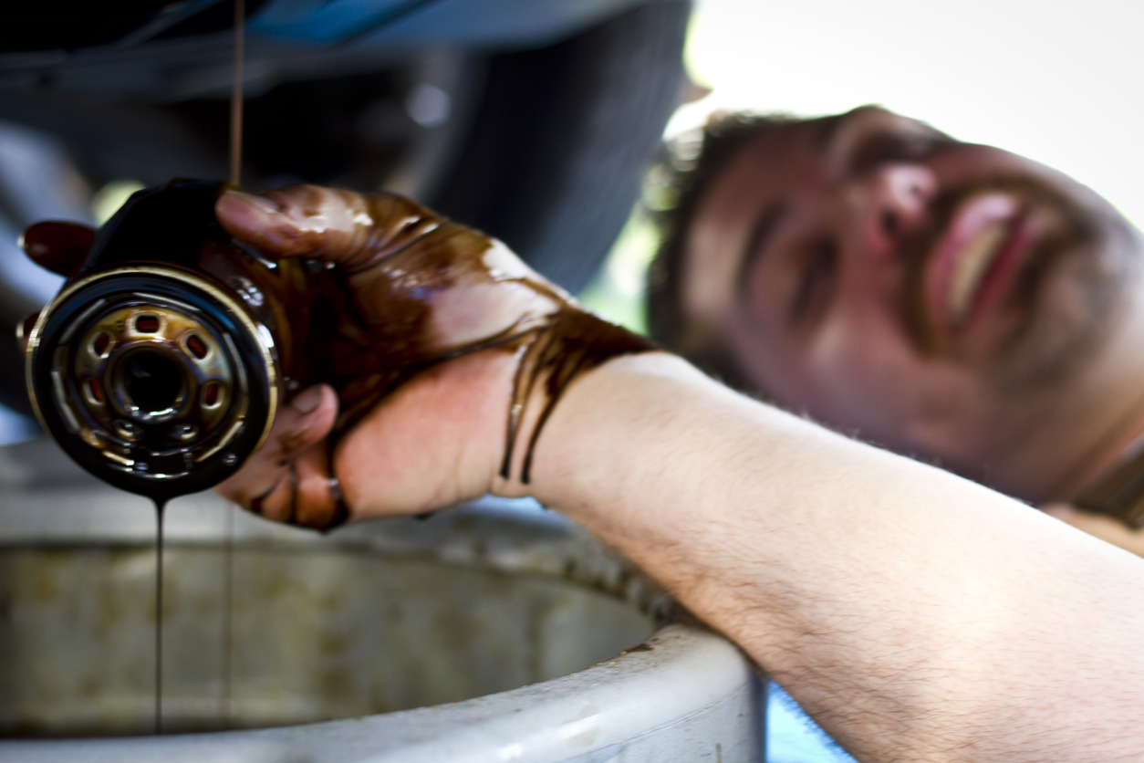 Tattooed mechanic with a mustache working on a car get oil on his hand.