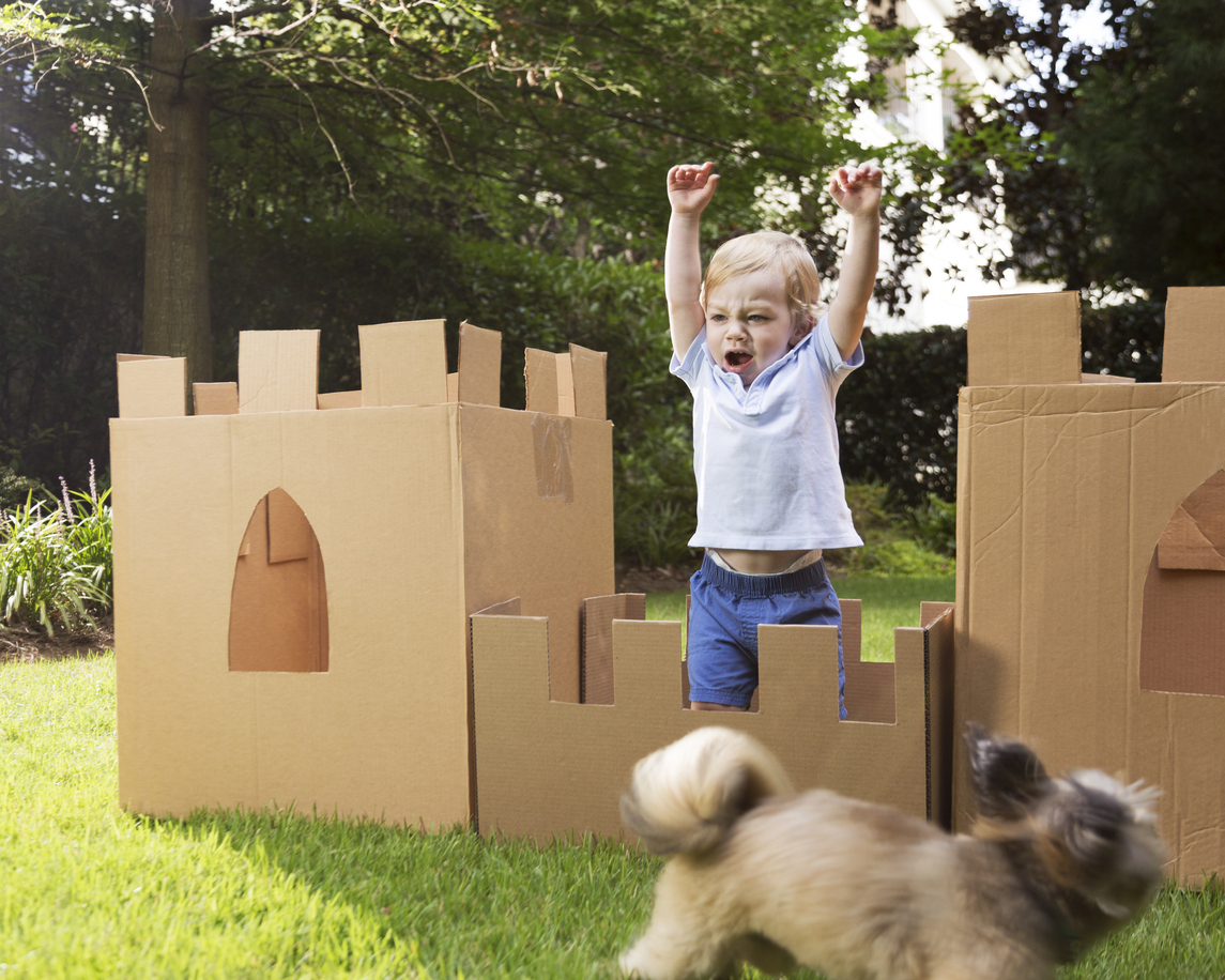 A little boy plays in a castle made from cardboard boxes.