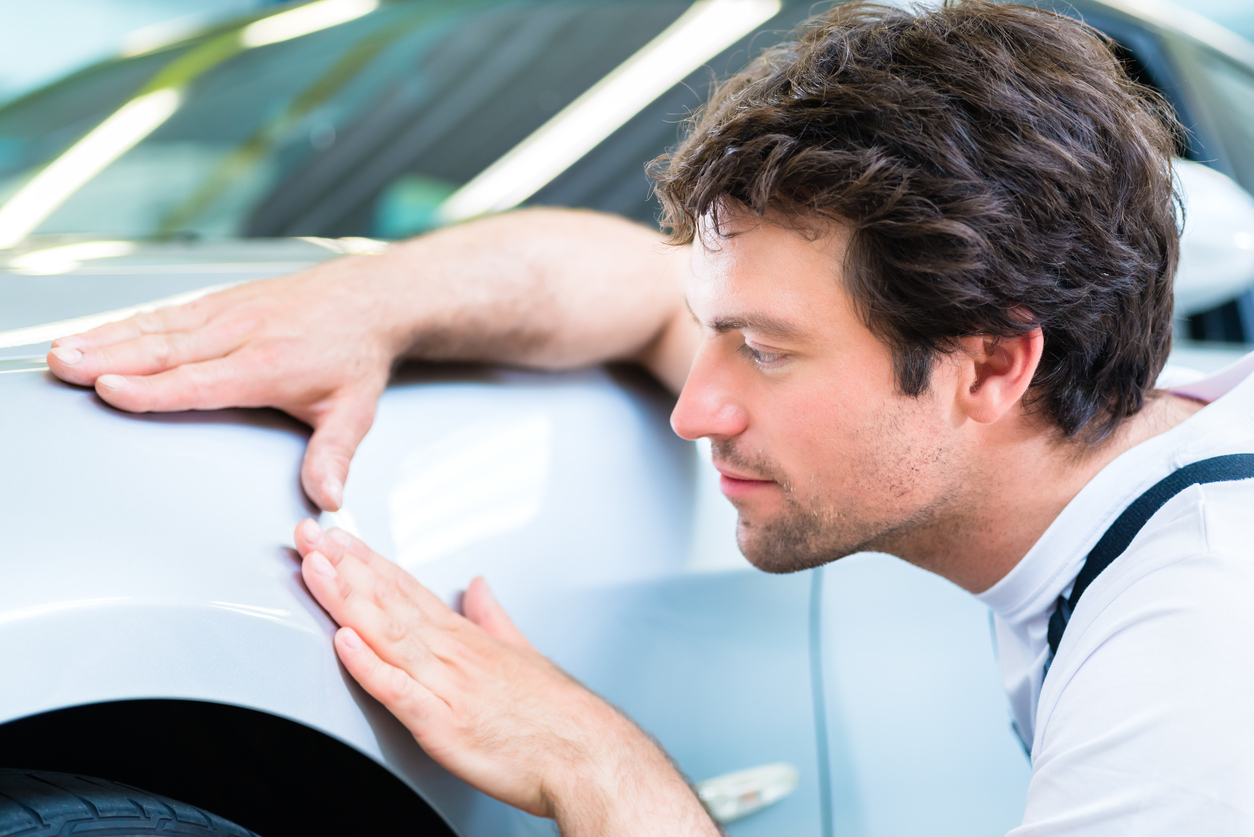 Male mechanic examine car finish on dents or scratches in workshop.