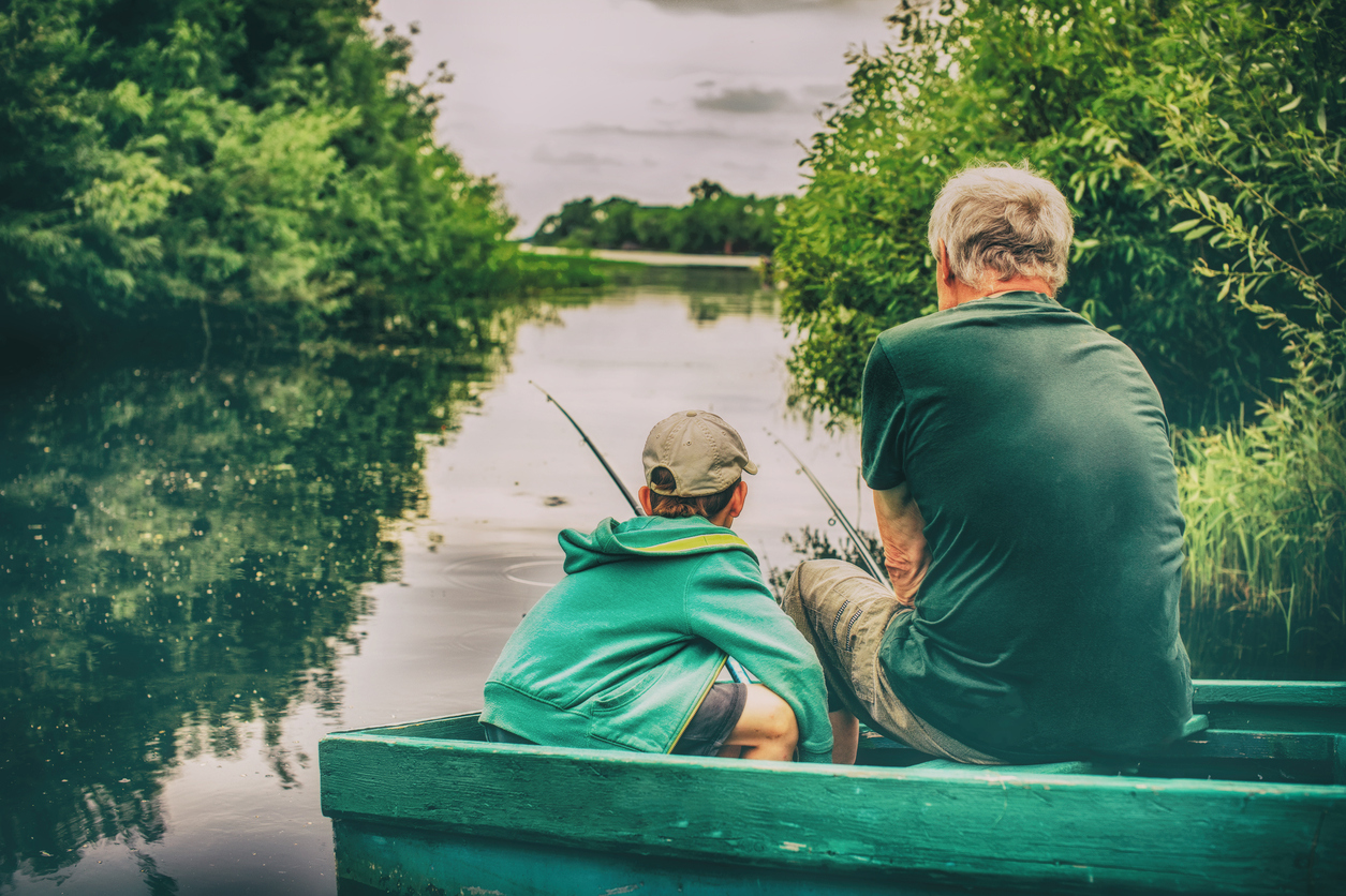Boy and grandfather sitting in a boat with a fishing rod.