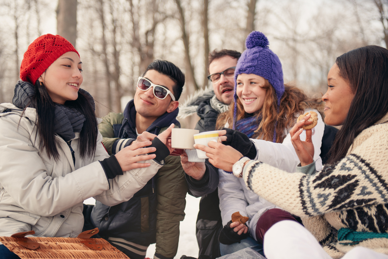 Group of millenial young adult friends enjoying wintertime and in a snow filled park.