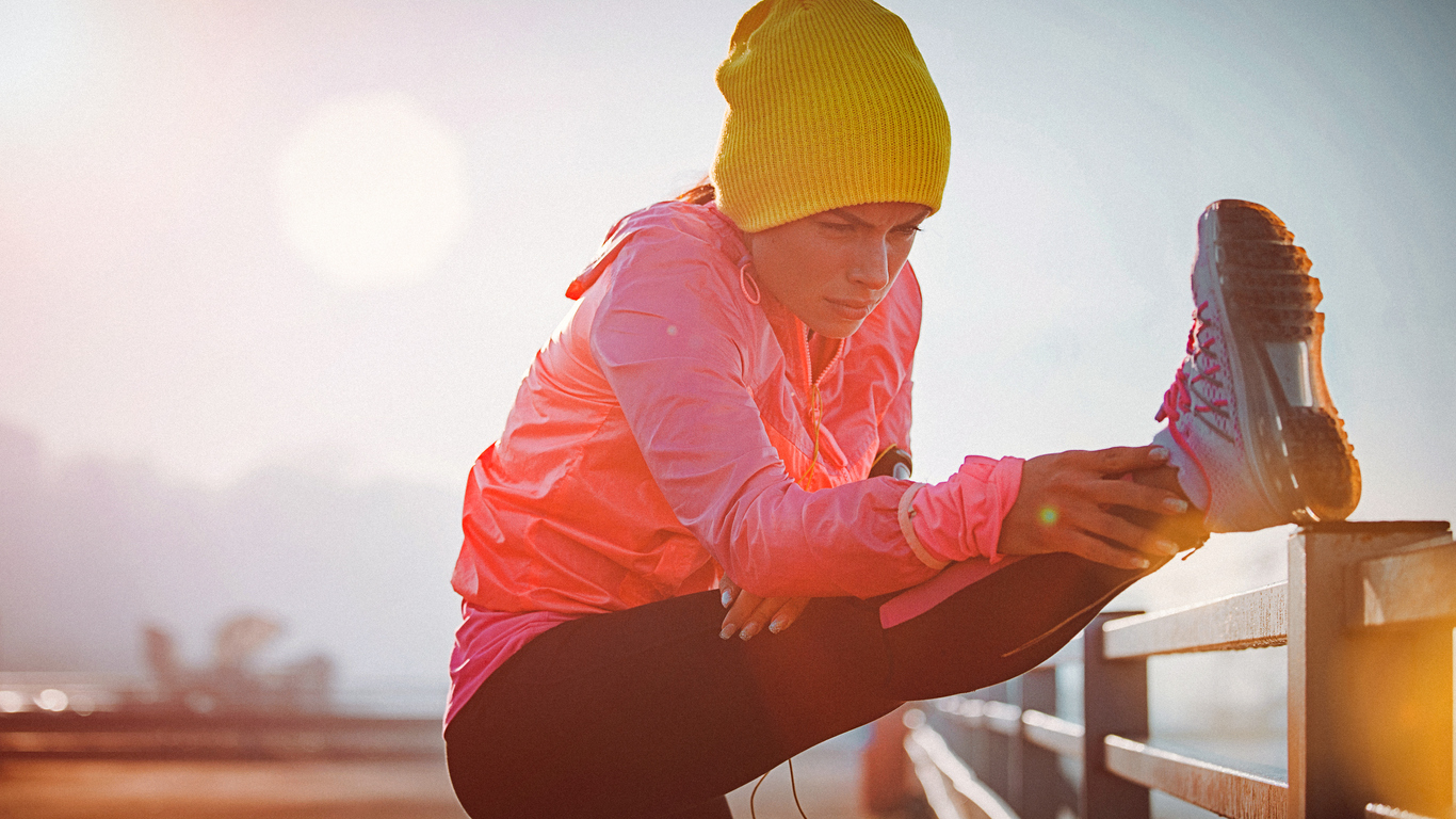 Front view of a young fit woman stretching her leg after running in the city port.