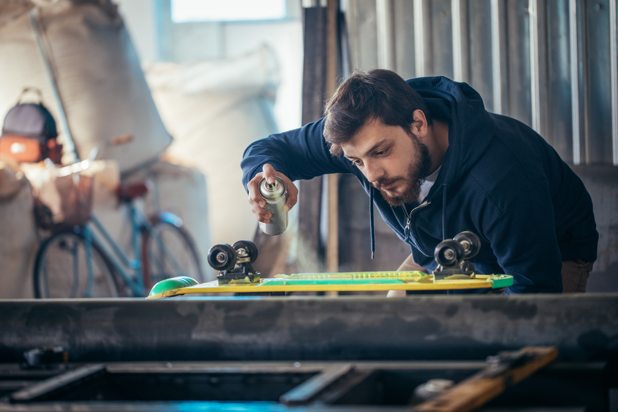 Young man in his workshop spray painting his skateboard.