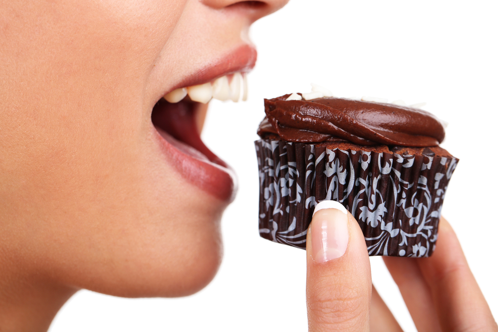 A woman poised to eat a chocolate cupcake to satisfy a craving.