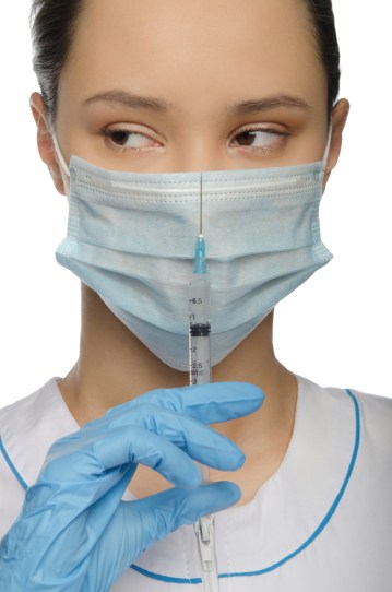 A doctor looks slyly to the left as she holds a syringe.