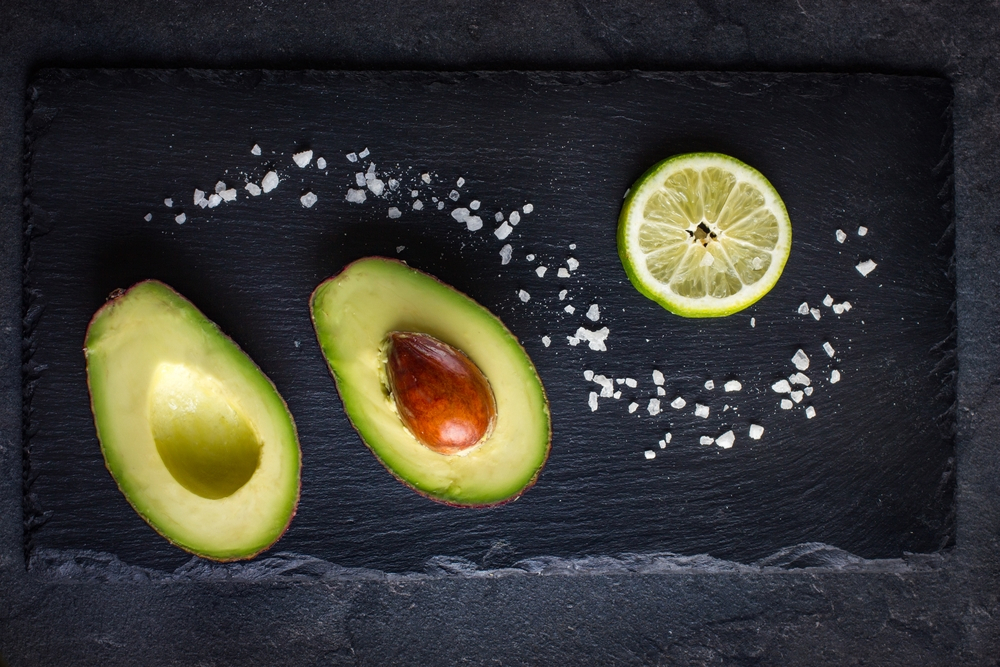 A halved avocado beside sea salt and sliced lime.