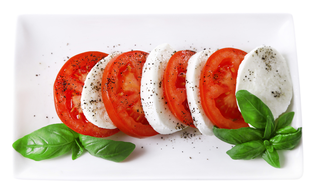 Slices of tomato and mozzarella on a plate with salt, pepper, and basil.