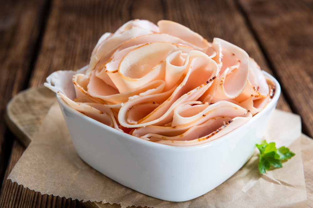 A white, square bowl with ruffled slices of turkey deli meat.