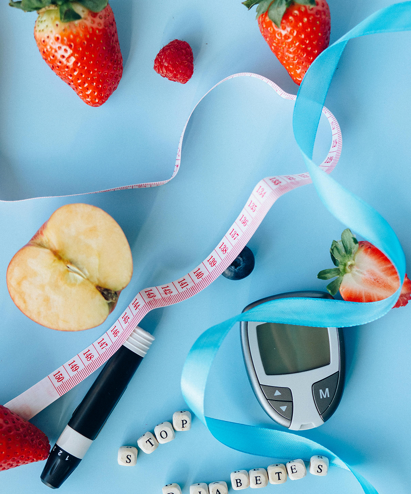 Fruits, a measuring tape, and a blood sugar monitor on a blue background.
